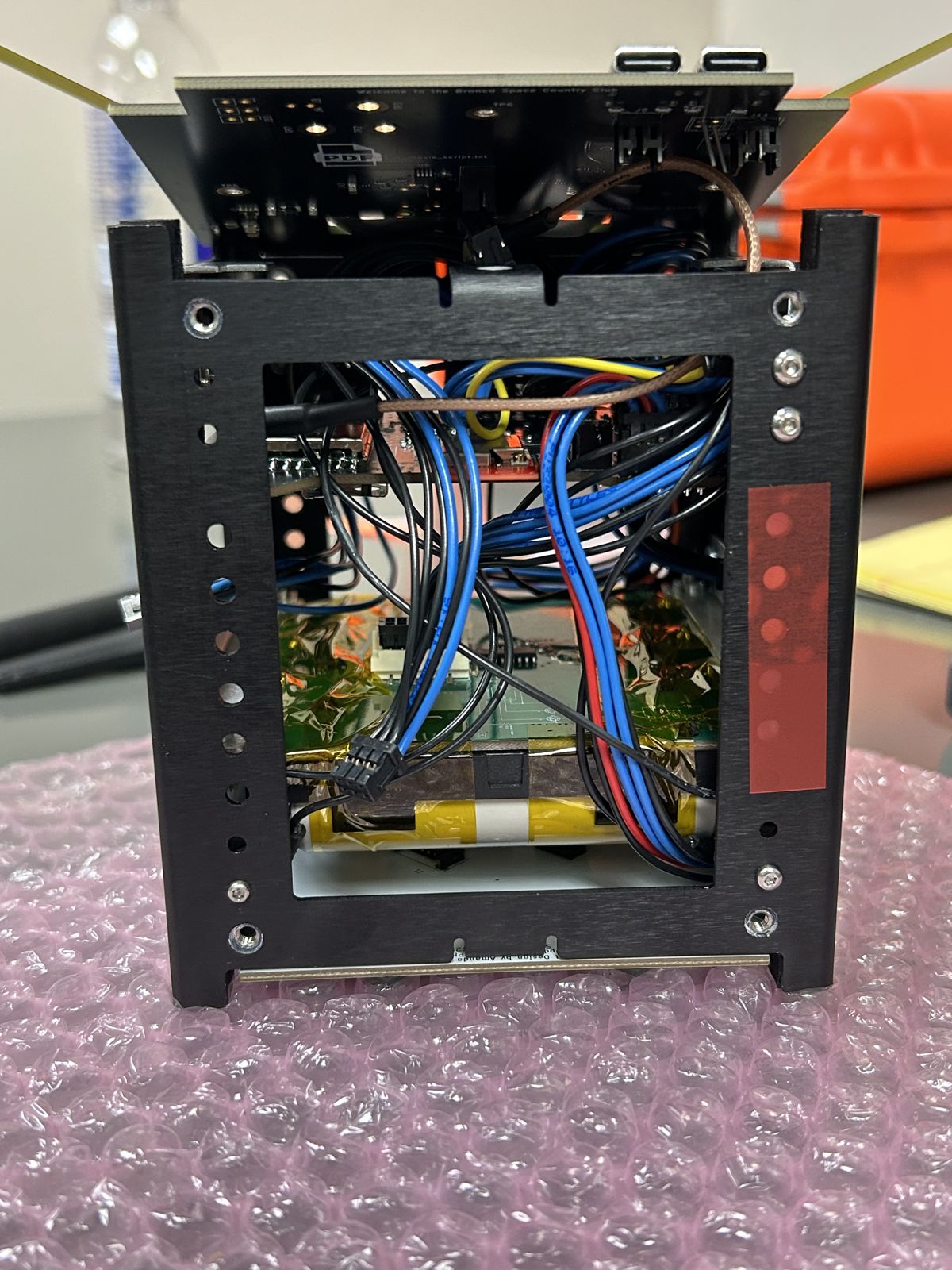 Open CubeSat frame showing internal wiring and the battery assembly