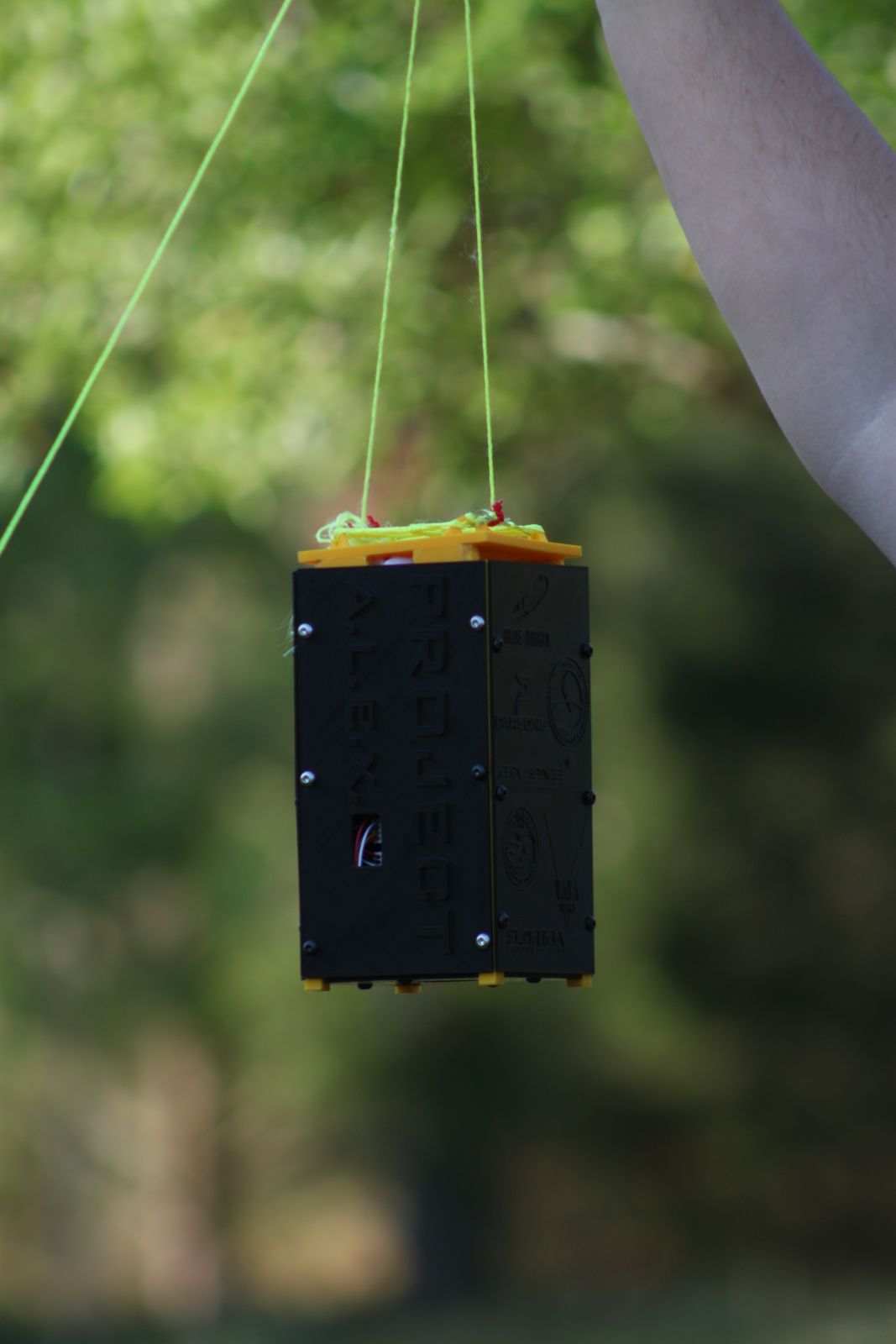 The black and yellow TSat-2A enclosure hanging from its tether lines outdoors